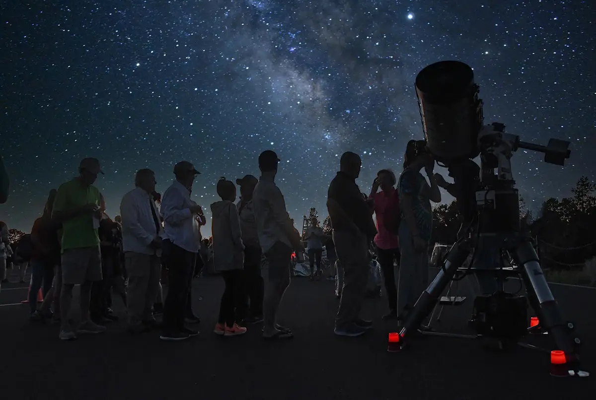 Personas observando el cielo nocturno junto a un telescopio